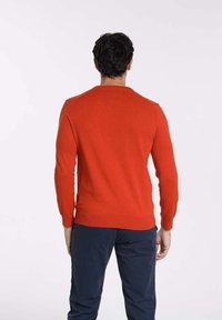 Pull en tricot rouge avec des manches longues, un col ras du cou, des poignets et un ourlet côtelés. Le tissu a une texture lisse et une coupe ajustée.