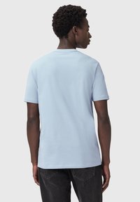 Lyseblå bomulds t-shirt med korte ærmer, rund hals og en glat tekstur. Bagsiden er ensfarvet med minimale sømme, parret med mørke jeans.