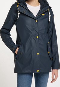 Veste de pluie marine avec extérieur imperméable, capuche à cordons, boutons-pression jaunes et poches latérales. Doublure intérieure douce visible.