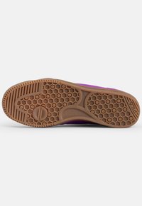 Sole di una sneaker viola con un motivo a nido d'ape e un grip testurizzato. Il materiale sembra gomma di colore marrone. Design robusto per una buona trazione.