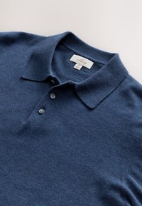 Marineblaues Poloshirt aus weichem Stoff, mit klassischem Kragen und Drei-Knopfleiste. Das Etikett trägt die Aufschrift „NEXT SIGNATURE“ und Größe M.