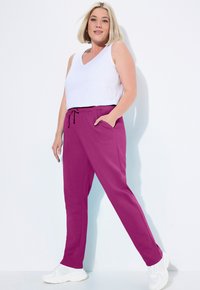 Pantaloni sportivi viola con vita regolabile e tasche laterali, abbinati a un top senza maniche bianco. Tessuto morbido, vestibilità comoda.