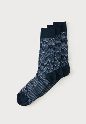 Drie paar donkerblauwe sokken met een zigzag- en gevlekt patroon, gestapeld gerangschikt op een witte achtergrond.