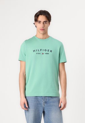 Mint green cotton T-shirt with short sleeves and a crew neck. Features navy "HILFIGER USA 1985" text with a small logo accent.