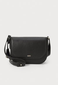 Borsa a tracolla in pelle nera con patta ripiegabile, dettaglio logo dorato e tracolla regolabile. Texture liscia, design minimalista, bordi arrotondati.