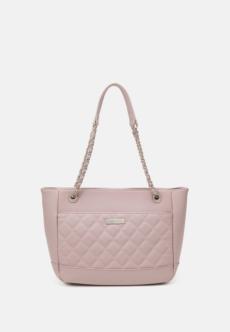 Sac fourre-tout rose pâle avec poche avant matelassée, anses en chaîne argentée et plaque de marque rectangulaire en métal.