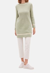 Abito maglione verde chiaro di maglia con una texture a coste e righe color crema ai polsini e all'orlo; abbinato a pantaloni bianchi a 3/4 e sneakers.