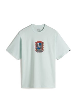 Camiseta de algodón verde menta clara con un gráfico de un esqueleto detrás de una pared de ladrillo rojo. Diseño de manga corta y cuello redondo.