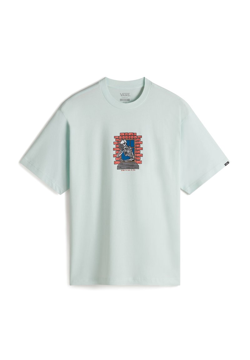 Camiseta de algodón verde menta clara con un gráfico de un esqueleto detrás de una pared de ladrillo rojo. Diseño de manga corta y cuello redondo.