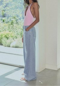 Vaaleanpunainen hihaton body, joka on yhdistetty löysiin vaaleansinihin farkkuihin. Asusteessa on taskut ja se on asetettu kirkkaaseen sisätilaan.