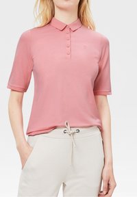 Polo à manches courtes rose clair avec col, patte de boutonnage à cinq boutons et petit logo. Associé à un pantalon à cordon de serrage beige clair.