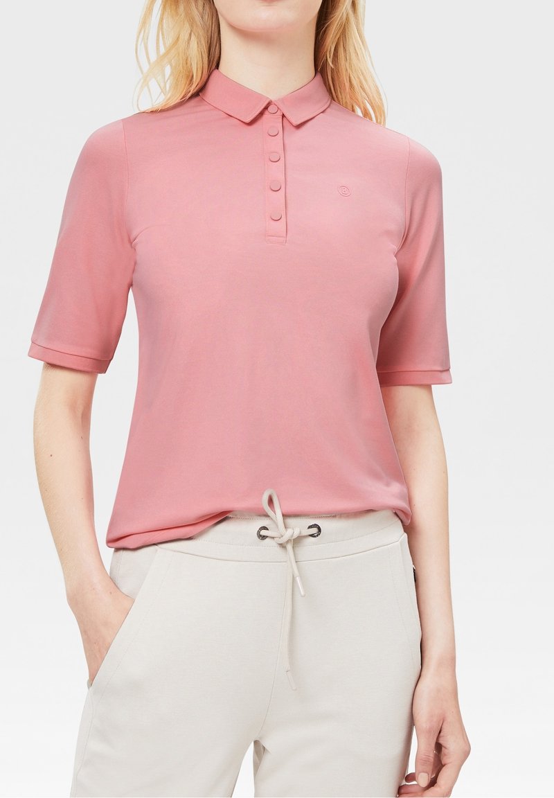 Polo à manches courtes rose clair avec col, patte de boutonnage à cinq boutons et petit logo. Associé à un pantalon à cordon de serrage beige clair.
