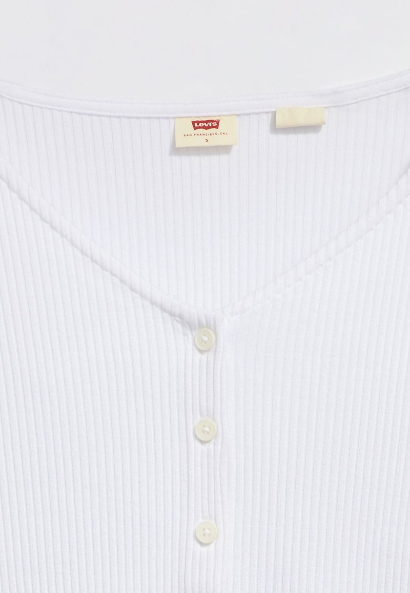 T-shirt bianco a coste con scollatura a V, dotato di tre piccoli bottoni chiari e di un'etichetta Levi's sulla parte sinistra del collo.