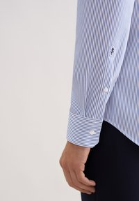 Camicia a righe blu e bianche con polsino a bottoni, realizzata in tessuto liscio. Presenta righe a contrasto e un orlo curato.