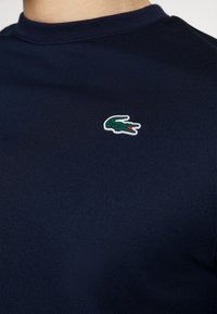 Navy blue short-sleeve t-shirt made of textured fabric, featuring a small green and red crocodile logo on the left chest.