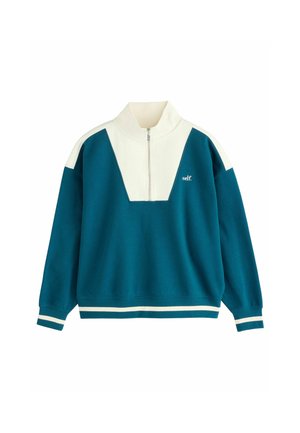Sudadera de color teal con cuello blanco y un diseño en forma de V en la parte delantera, que incluye una cremallera y el logo "self." en el pecho.