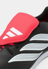 Μαύρο αθλητικό παπούτσι με υφή στην επιφάνεια, έντονη ροζ επένδυση στη γλώσσα και τρεις λευκές διαγώνιες ρίγες στο πλάι. Διαθέτει μαύρα κορδόνια.