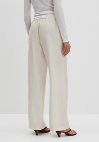 Light beige wide-leg pants with a textured finish, elastic waistband, and two back pockets, paired with brown heeled sandals.