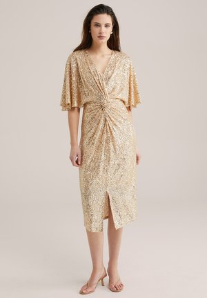 Gold sequin dress with short flutter sleeves, a twisted waist detail, knee-length hem, and front slit, paired with nude heeled sandals.
