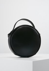 Round black leather bag with a smooth texture, flat base, and a top handle, featuring a minimalist design and no visible hardware.