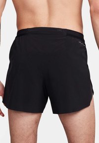 Shorts de sport noirs avec une texture lisse, dotés d'une taille en mesh, de fentes sur les côtés et d'une petite poche à l'arrière. Tissu respirant conçu pour le confort.