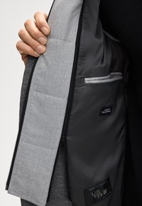 Wnętrze szarej kurtki pokazujące jasno szare podszewkę z kieszenią zapinaną na suwak. Charakteryzuje się gładką teksturą i kontrastującymi czarnymi krawędziami.