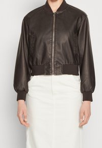 Hnědá umělá kožená bomber bunda se zipem vpředu, žebrovanými manžetami a zkráceným střihem, kombinovaná s bílou sukní.