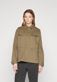 Olive green military-style jacket made of cotton. Features two chest pockets and two side pockets, with a collared neckline and button closure.