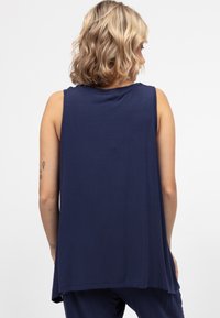 Bezs rękawów granatowa bluzka z miękkiego materiału, o luźnym kroju i zaokrąglonym dołem. Tylny design ukazuje gładką teksturę z minimalnym zdobieniem.