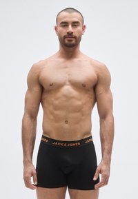 Boxer noir avec une ceinture orange portant le texte "JACK & JONES". Tissu lisse, coupe ajustée et jambes courtes.