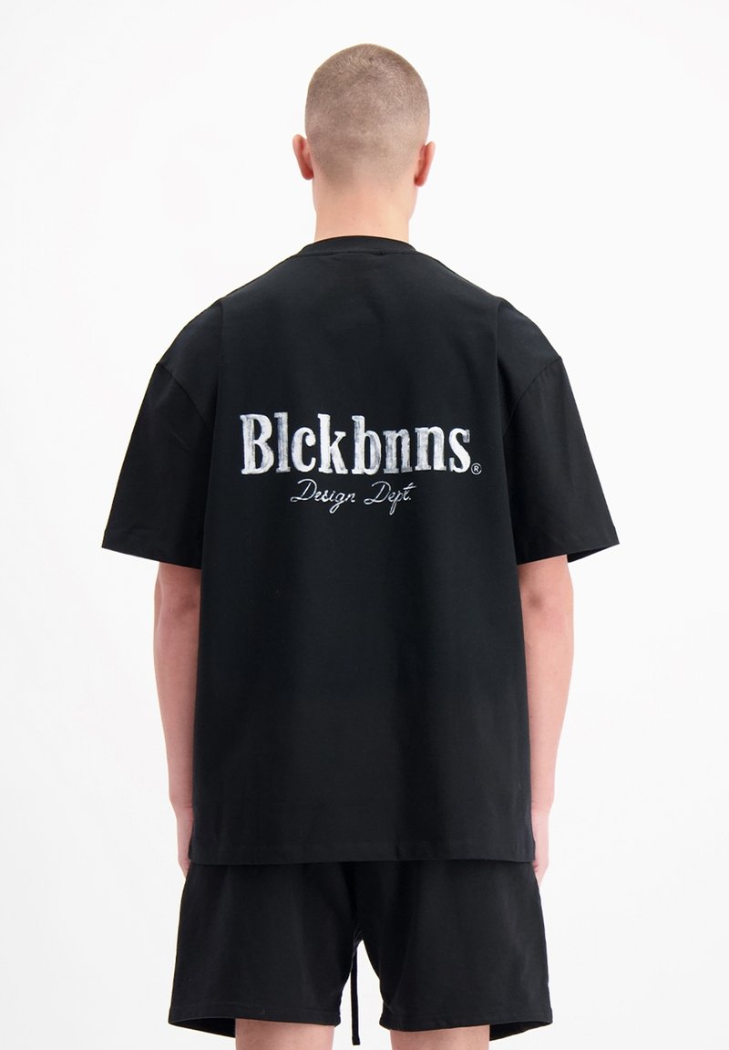 Zwarte katoenen T-shirt met grote witte geborduurde tekst op de achterkant: "Blckbnns Design Dept." Korte mouwen en een ontspannen pasvorm.