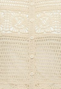 Tissu en crochet couleur crème avec motifs floraux, fermeture verticale par boutons et motif en maille ouverte dans la partie inférieure.