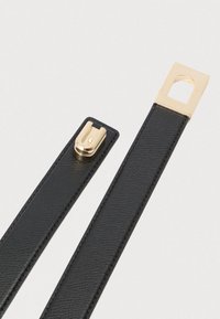 Melns ādas siksniņa ar zelta metāla sprādzi un taisnstūra formas izgriezumu, kas atklāj gludu tekstūru un precīzu šuvumu.