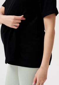 Sort kortærmet top med en løs pasform, der har en samlet sektion i siden, parret med lysegrønne ribbede leggings.