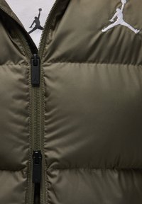 Olive green puffer vest featuring a full zipper, black zipper pull, and a white embroidered Jumpman logo on the upper left side.