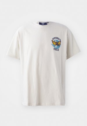 Krémszínű pamut póló rövid ujjakkal, színes sas grafikával és "SUPERBIA IN PROELIO" felirattal a bal mellen.