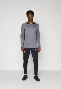 Šedé atletické tričko s dlhým rukávom s čiernymi akcentmi a okrúhlym výstrihom, kombinované s čiernymi zúženými nohavicami a čiernymi atletickými topánkami.