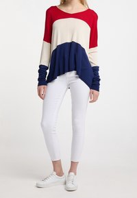 Haut à rayures rouge, crème et marine à manches longues avec un ourlet arrondi, associé à un jean skinny blanc et des baskets blanches. Matériau en tricot léger.