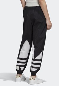 Svart och vit träningsoverall med ett lätt, skrynkligt tyg. Har stora vita detaljer och tre horisontella svarta ränder vid fållarna.