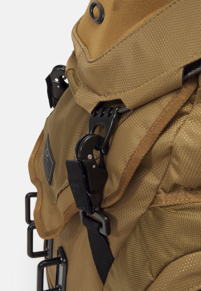 Zaino in tessuto beige con superficie texture, dotato di accessori neri, spallacci regolabili e una chiusura a patta prominente con gancio.