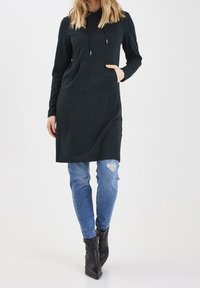 Svart huvtröja med lång ärm och ficka fram, ihop med slitna ljusblå jeans och svarta anklarstövlar.