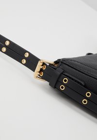 Bolso de hombro de cuero negro con acabado texturizado y herrajes dorados. Cuenta con una correa con remaches decorativos y un detalle de hebilla ajustable.