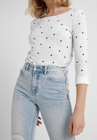 Vit långärmad topp med marinblå stjärnmönster, kombinerad med ljusblå högmidjade jeans med slitningar vid knäna.