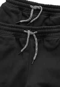 Schwarze Jogginghose aus weichem Stoff, mit einem elastischen Bund, grauem geflochtenem Kordelzug und seitlichen Taschen für zusätzlichen Komfort.