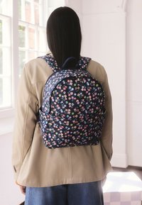 Virágmintás sötétkék hátizsák párnázott vállpántokkal, lekerekített formával, cipzáras záródással és oldalzsebekkel. Tartós anyagból készült.