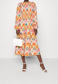 Farverig mønstret kjole med lange ærmer og en samlet talje, lavet af letvægtsstof. Sæt sammen med en hvid håndtaske og hæle.