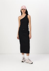 Black one-shoulder top paired with a long black cargo skirt. Accented with a pink cap and light pink sneakers with black soles and white socks.