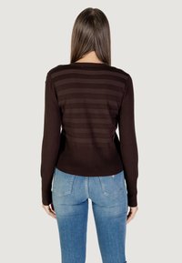 Suéter marrón con rayas horizontales en la parte trasera y un dobladillo acanalado. Combinado con jeans de un azul claro, que presentan una silueta ajustada.