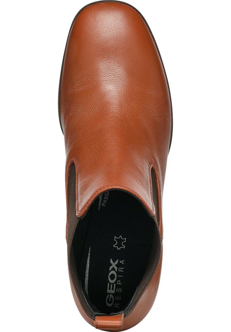 Chaussure à enfiler en cuir marron avec des panneaux latéraux élastiques, bout arrondi et logo embossé sur la semelle intérieure. Texture lisse et design minimaliste.