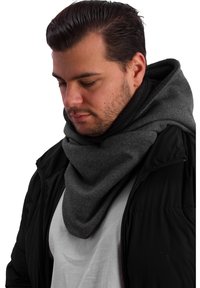 Dark grey triangular scarf made of soft fabric, layered around the neck. Worn over a white shirt and black jacket. Smooth texture, minimal design.